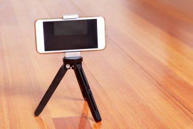 Cep telefonu hafif ahşap yüzeyde tripodun üzerinde duruyor ve ateş etmeye hazırlanıyor. Akıllı telefon kullanarak video, fotoğraf ya da video kaydı yapmak. İçerde, boşluğu kopyala.