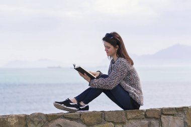 Bir kız dinlendikten ve deniz kenarında okuma