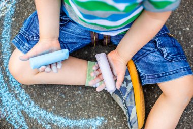 Sevimli erkek ve kız parkta kaldırımda tebeşir ile çizim. Çocuklar için yaz etkinlikleri. Bir çocuk mavi tebeşir ile yaratıcı çizim yolda.
