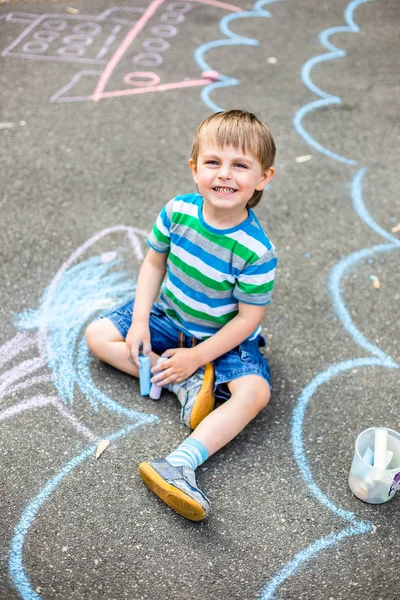 Cute boy and girl drawing with chalk on the sidewalk in the park. Summer activities for children. Creative drawing of a child with blue chalk on the road.