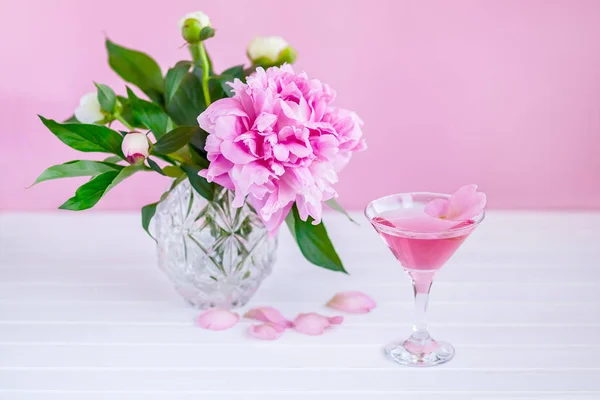 Pink peony next to glass of pink wine. pink background