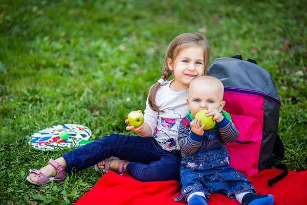 A small child bites a large green apple and holds it in his hands.