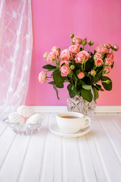 A cup of tea, candy and a bouquet of roses on a pink background. Cozy home.