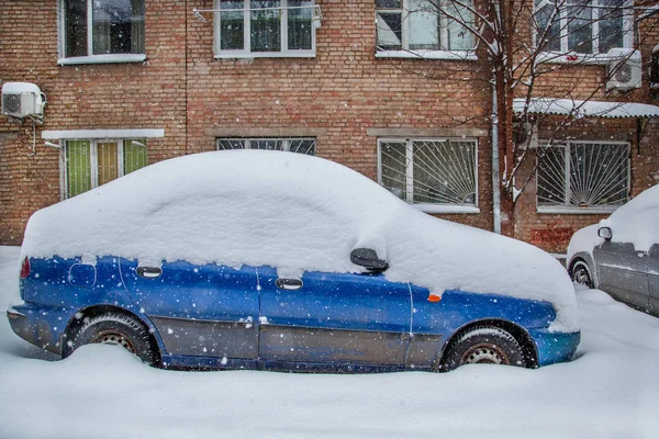 Vehicles covered with snow in a winter blizzard in the parking lot. Snow-covered roads and streets of the city.