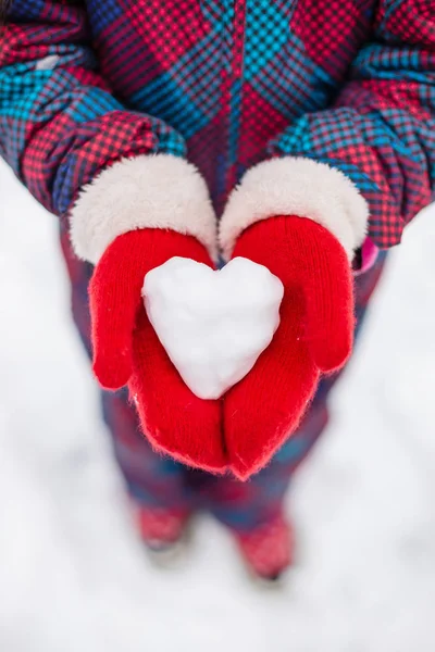 A girl in red gloves holds a heart shaped snowball. Symbol of love for Valentine\'s Day.