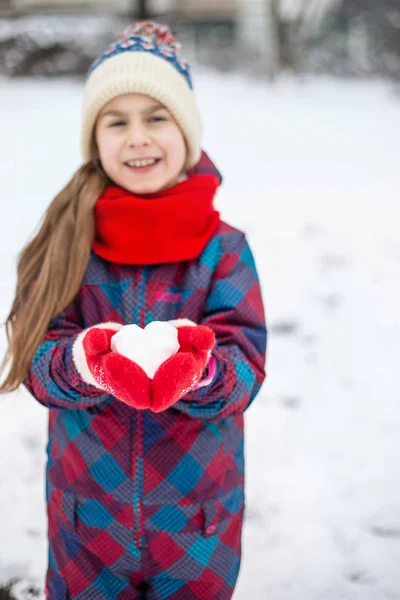 A girl in red gloves holds a heart shaped snowball. Symbol of love for Valentine\'s Day.