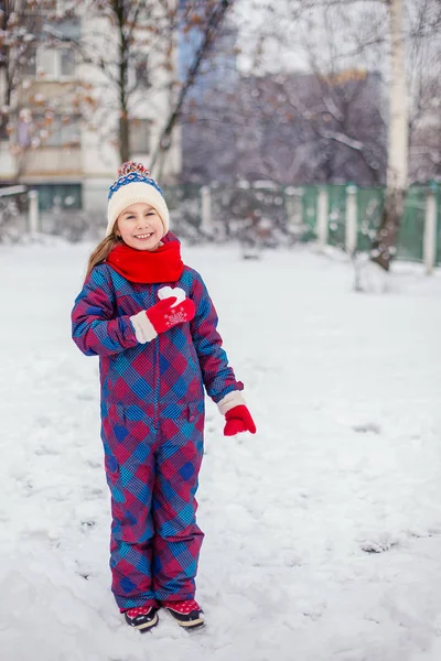 A girl in red gloves holds a heart shaped snowball. Symbol of love for Valentine\'s Day.