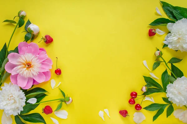 Flowers of peony, branches, leaves and petals and berries of cherry, strawberry with space for text on a yellow background. Flat lay, top view. Peony flower texture.