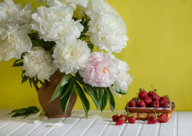 Peonies kil vazo ve bir kase Çilek ağacı masada büyük bir buket. Romantik ruh hali.