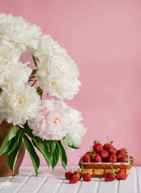 Peonies kil vazo ve bir kase Çilek ağacı masada büyük bir buket. Romantik ruh hali.