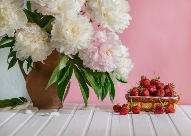 Peonies kil vazo ve bir kase Çilek ağacı masada büyük bir buket. Romantik ruh hali.