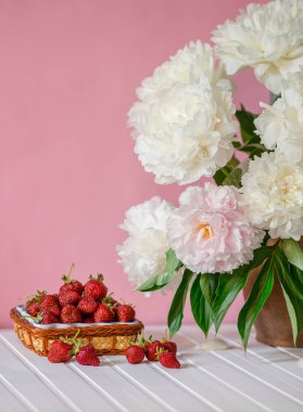 Peonies kil vazo ve bir kase Çilek ağacı masada büyük bir buket. Romantik ruh hali.