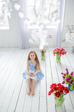 Güzel mavi gözlü kız, bahar çiçekleri parlak bir odada arasında küçük bir kız portresi.