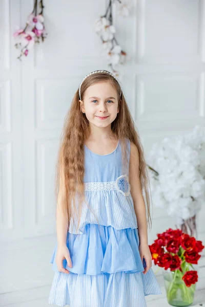 Portrait d'une belle fille aux yeux bleus, une petite fille parmi les fleurs du printemps dans une pièce lumineuse . — Photo