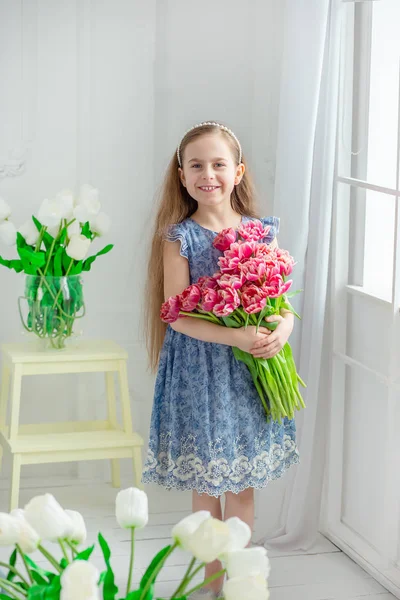 美しい青い目の少女、明るい部屋の春の花の中で少女の肖像画. — ストック写真