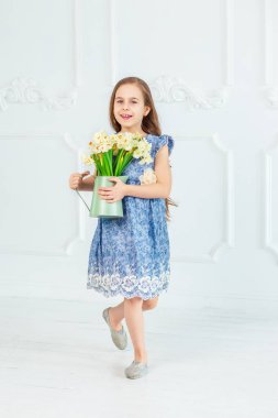 Güzel mavi gözlü kız, bahar çiçekleri parlak bir odada arasında küçük bir kız portresi.