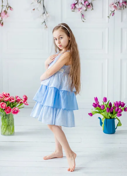 美しい青い目の少女、明るい部屋の春の花の中で少女の肖像画. — ストック写真