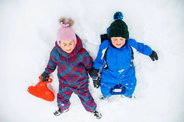 Fratello e sorella felici sdraiati sulla neve. Giochi invernali all'aria aperta . — Foto Stock