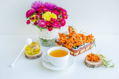 Beyaz arka plan, doğal ışıklandırma. Deniz dikeni meyveleri, kekik ve bal ile sıcak tatlı organik çay.