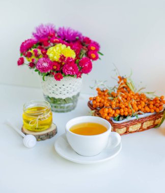 Beyaz arka plan, doğal ışıklandırma. Deniz dikeni meyveleri, kekik ve bal ile sıcak tatlı organik çay.