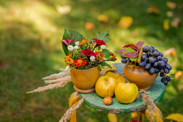 Autumn composition with grapes, quince and flowers located in the garden on a blurred green natural background.