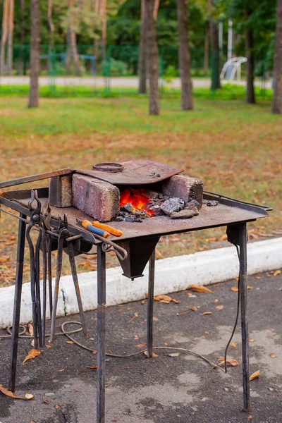 A blacksmith forges a metal blank on the anvil at a fair in the presence of spectators.