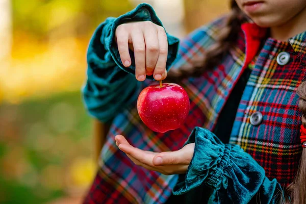 A girl holding a red apple in her hands in the autumn garden on a blurred background, place for text. — Stock Photo, Image