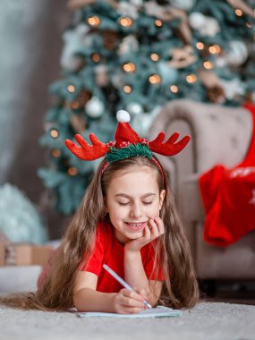Noel Baba şapkalı tatlı bir kız Noel ağacının yanında Noel Baba 'ya mektup yazıyor. Mutlu çocukluk, arzularını tatmin etme zamanı. Mutlu Noeller..