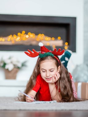 Noel Baba şapkalı tatlı bir kız Noel ağacının yanında Noel Baba 'ya mektup yazıyor. Mutlu çocukluk, arzularını tatmin etme zamanı. Mutlu Noeller..
