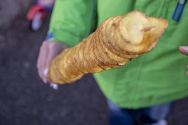 Yeşil ceketli bir çocuk bir şiş patates kızartması ile bir sopa yiyor.