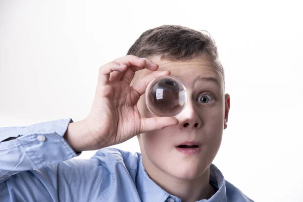 男孩拿着一个玻璃球在他的眼睛前面 你看到他的眼睛扩大 — 图库照片