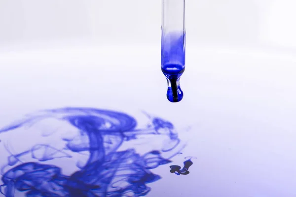 ピペットの青い液体で水に水滴がしたたり — ストック写真