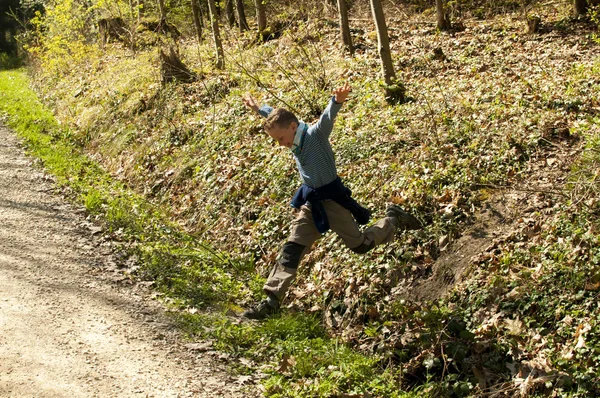 Niño salta con un gran salto sobre una zanja en la ruta de senderismo en el bosque —  Fotos de Stock