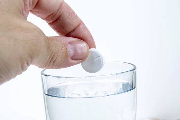 Hand throws an effervescent tablet into a glass of water against a white background