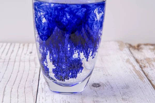 Blue liquid spreads in a glass full of water — Stock Photo, Image