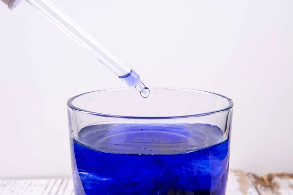 Pipetta sopra un bicchiere con liquido blu in laboratorio — Foto Stock