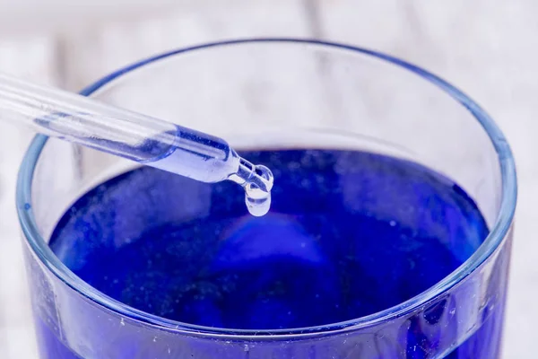 Пипетка сбрасывает каплю жидкости в синий контейнер с жидкостью — стоковое фото