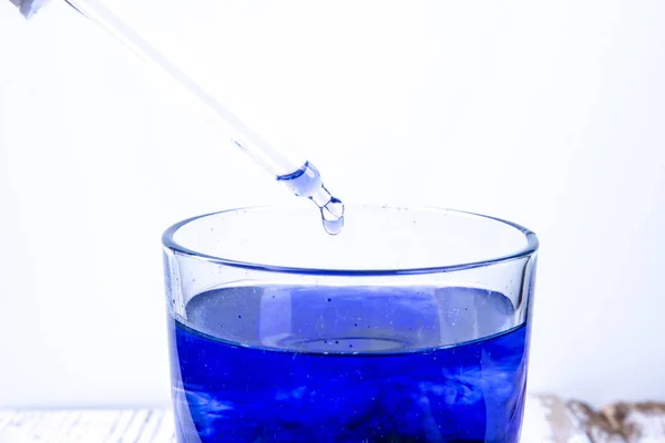 Pipetta sopra un bicchiere con liquido blu in laboratorio — Foto Stock