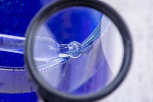 Труба под увеличительным стеклом над голубым жидким стеклом — стоковое фото