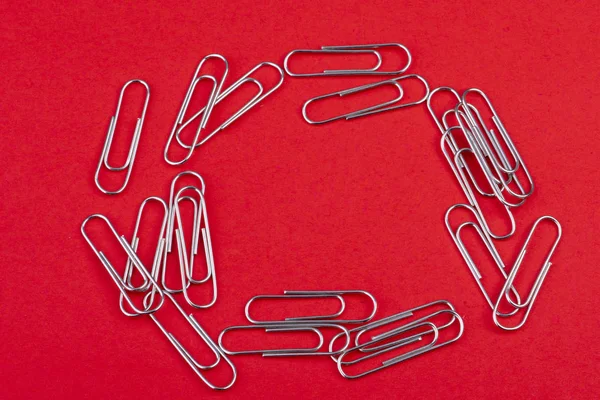 Paperclips ułożone w kółko na czerwonym tle — Zdjęcie stockowe