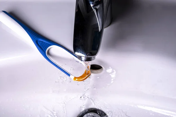 Tongue cleaner under the running water in the wash basin at the water tap