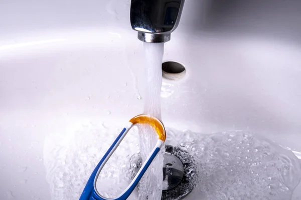 Tongue cleaner under the running water in the wash basin at the water tap