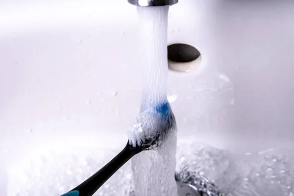 Зубна щітка очищається в раковині під проточною водою — стокове фото