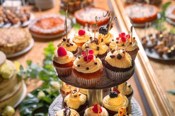 sweet table at a wedding with sweet muffins cream filling and garnished with fruits in front of a mirror