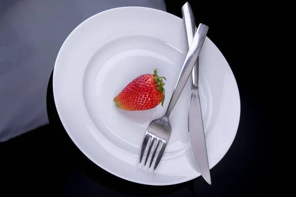 Одинокая клубника на белой тарелке со столовыми приборами как диетический план — стоковое фото