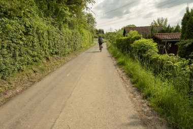 Bisikletçi çalıların kenarında bir fırtına gökyüzü altında yalnız bir yolda sürme
