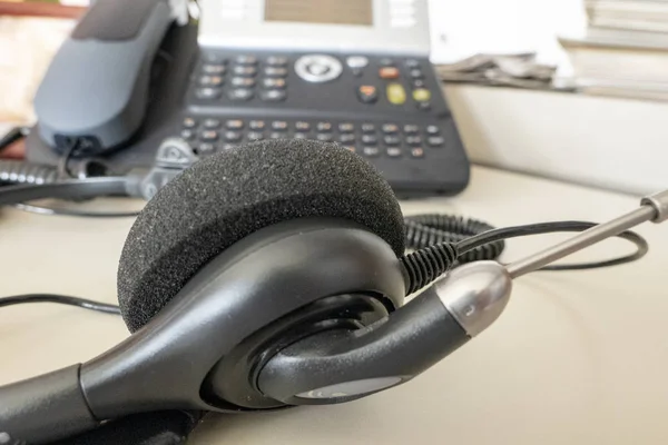 Masanın üzerinde ofiste arka planda telefon bulunan kulaklık — Stok fotoğraf
