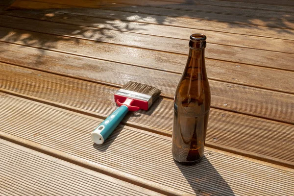 Botella de cerveza vacía y un cepillo están tumbados en la terraza medio empotrada con esmalte — Foto de Stock