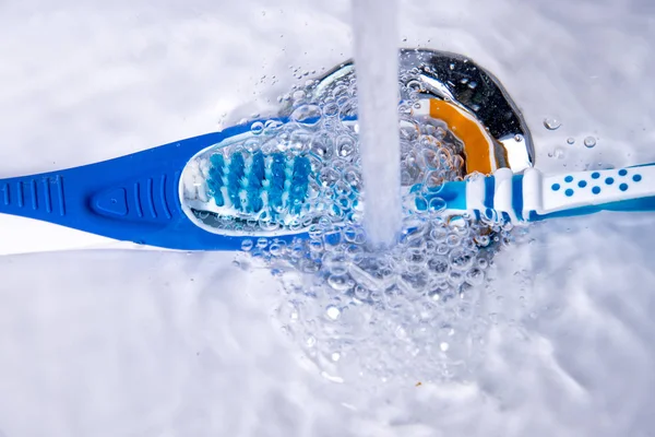 Tongue cleaner and toothbrush under running water in the bathroom — Stock Photo, Image