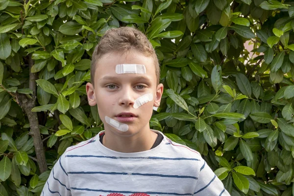 Menino com gesso no rosto na frente de uma sebe parece triste — Fotografia de Stock